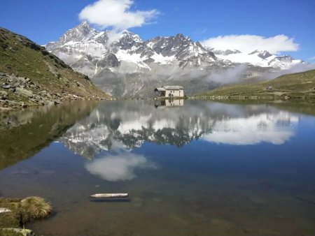 Bergmeer met een grasoever en wandelaars op de dam – 5-Merenroute vanaf Sunnegga, Zermatt